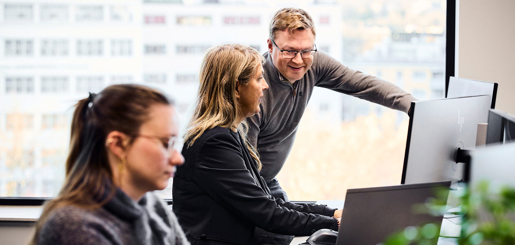 Team collaborating at office computers in modern open workspace with city view.