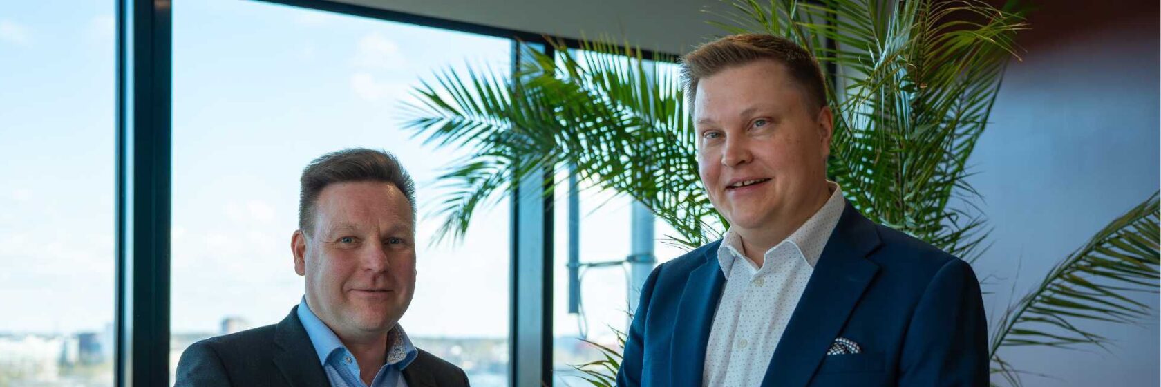 Swecon toimialajohtajat Mikko Turunen ja Tuomas Salminen valoisan ikkunan edessä hymyilemässä.