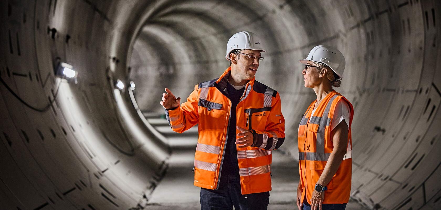 Engineers in orange safety gear inspecting a concrete tunnel construction site.