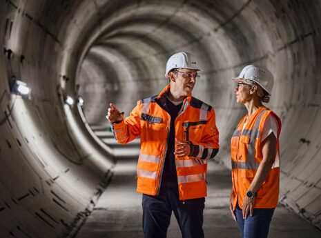 Engineers in orange safety gear inspecting a concrete tunnel construction site.