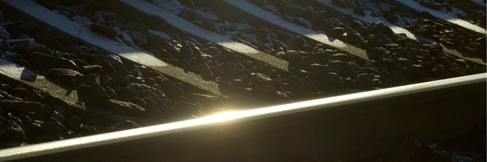 Lähikuva junaraiteesta, kiskolla paistaa aurinko.