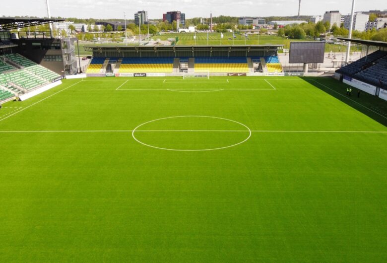 Tyhjä jalkapallostadion ja vihreä nurmikenttä aurinkoisena päivänä.
