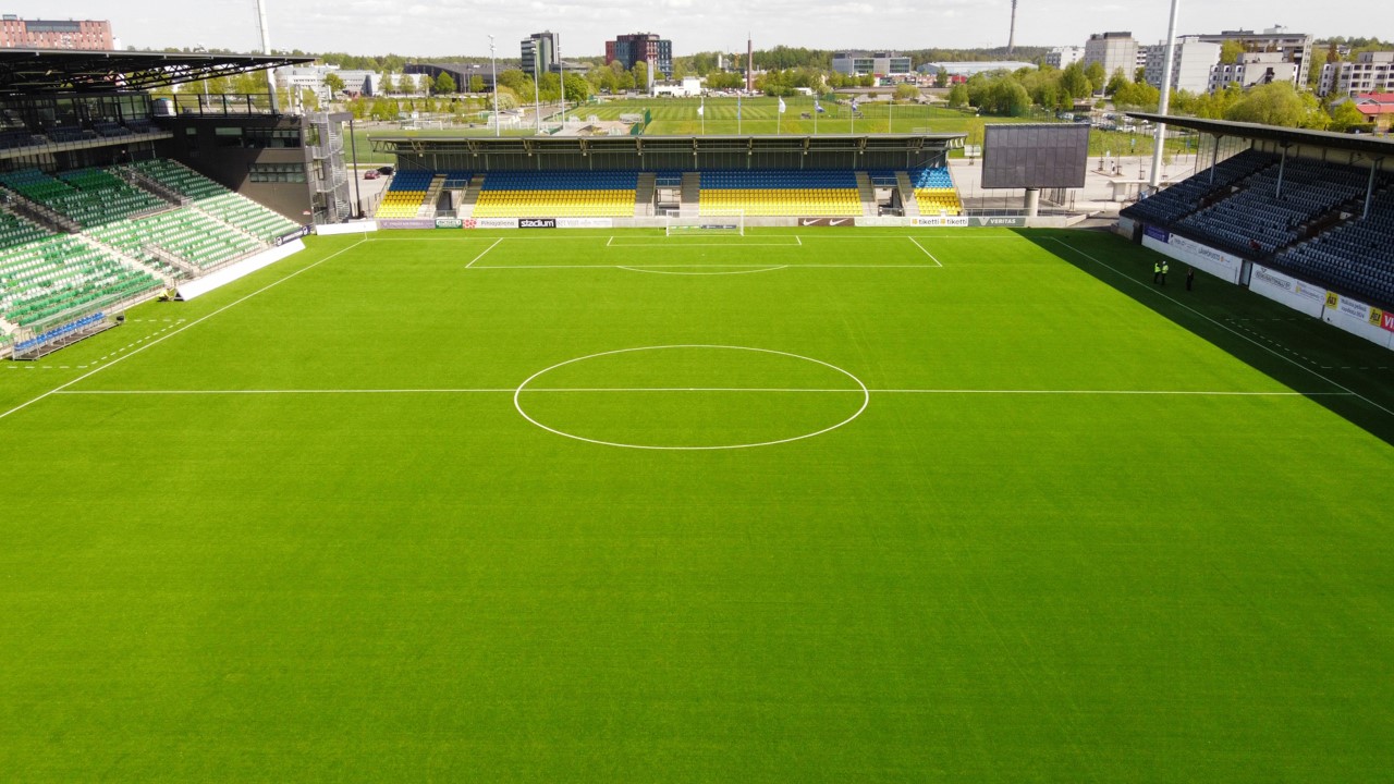 Empty football stadium with green pitch and colorful seating under bright daylight