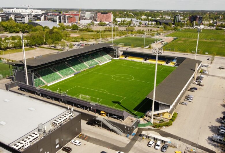 Aerial view of a modern football stadium with green pitch and city buildings around