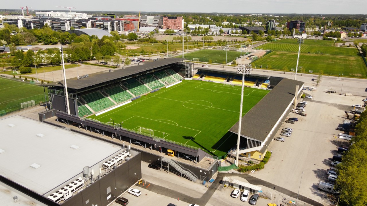 Aerial view of a modern football stadium with green pitch and city buildings around