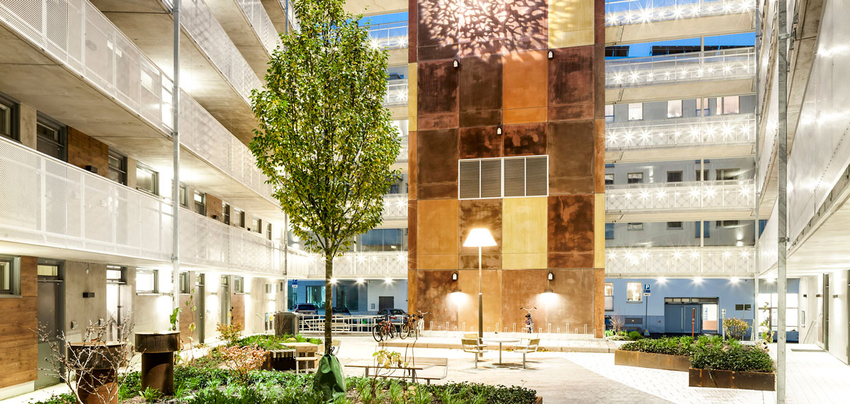 Modern apartment courtyard with central tree, benches and warm architectural lighting.