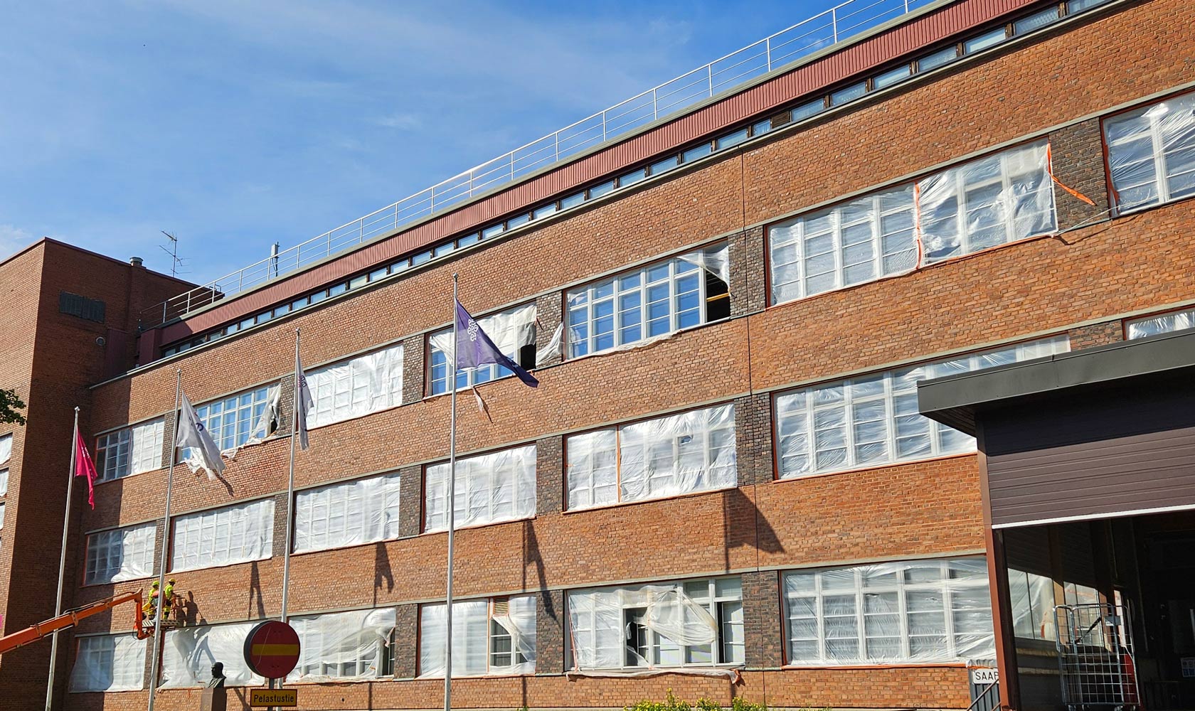Tiilirakennuksen julkisivuremontti, ikkunat suojattu muovilla ja työmaa nosturilla.