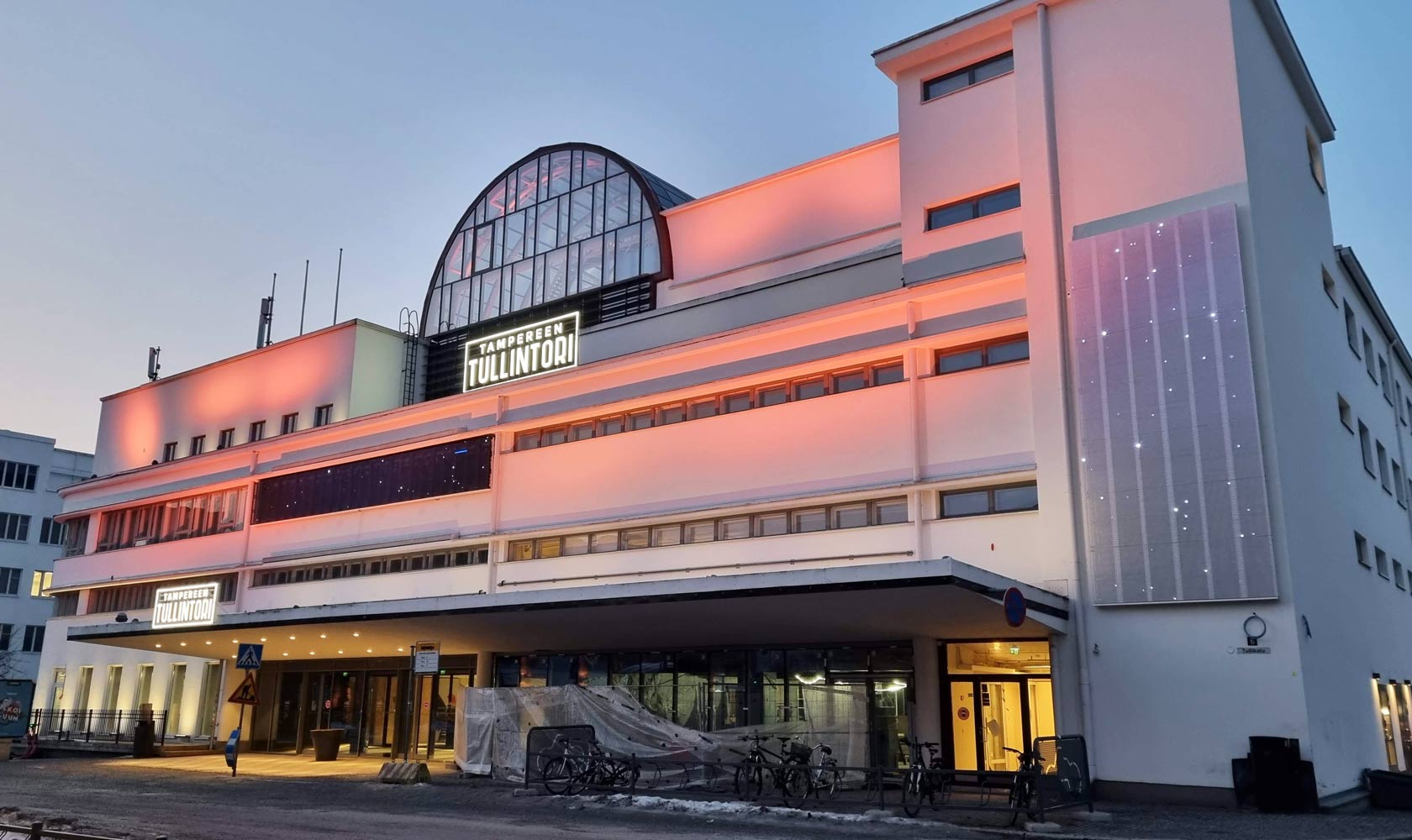 Tampereen Tullintori -kauppakeskus iltavalaistuksessa, moderni valkoinen rakennus.