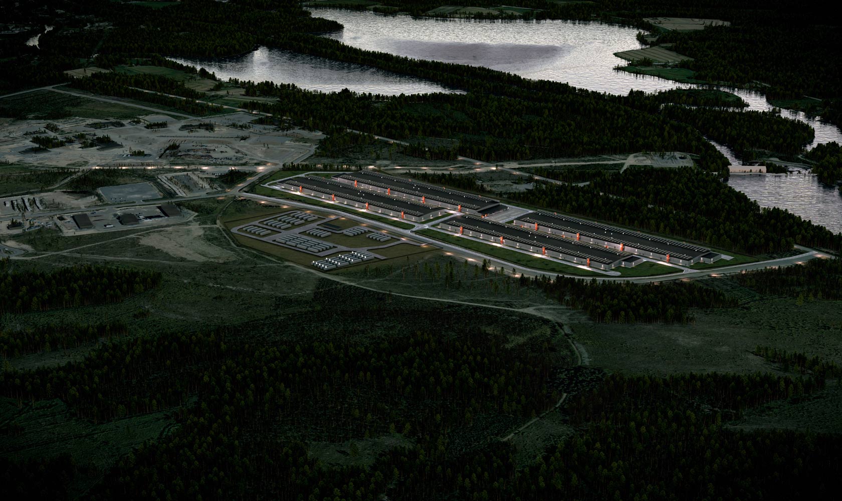 Ilmakuva teollisuusalueesta järven rannalla, valaistu tehdas ja metsää ympärillä.