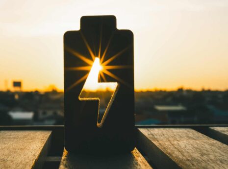 Battery icon silhouette with lightning bolt at sunset, renewable energy charging concept.