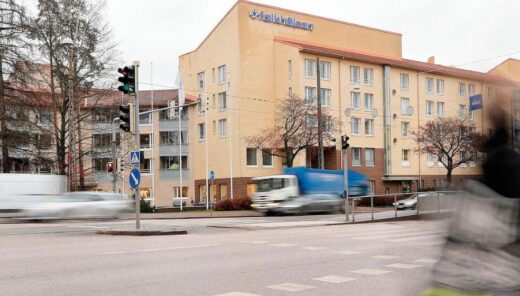 Keltainen Folkhälsan -talosta kuvattuna Mannerheimintieltä, etualalla liikkeestä blurraantunut jalankulkija.