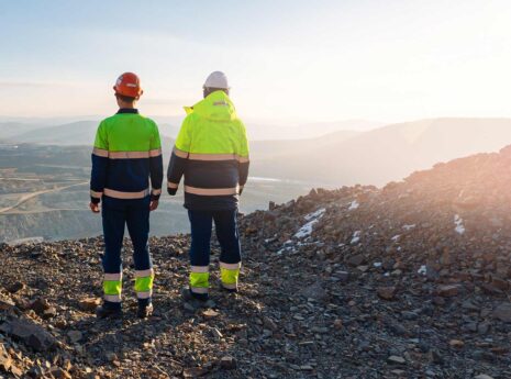 Two mining workers in safety gear overlooking an open pit mine at sunrise.