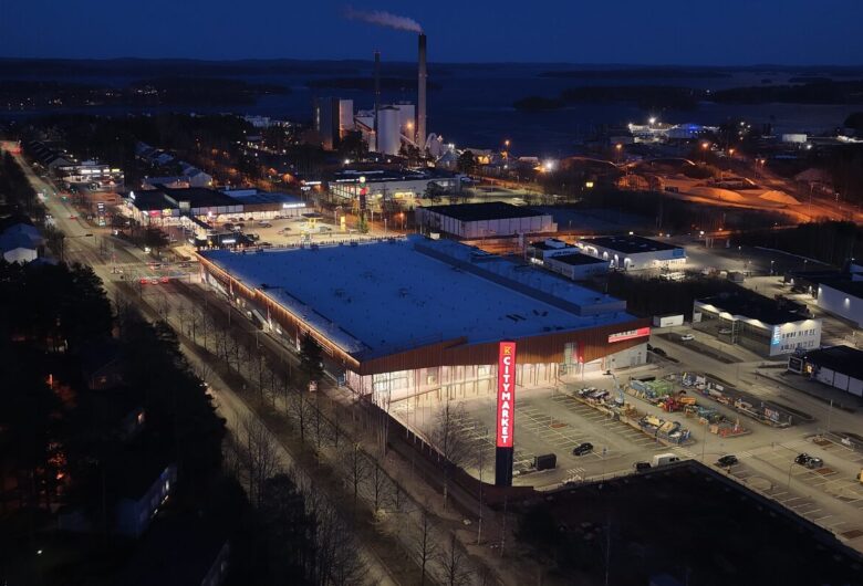 Pimeällä otettu ilmakuva kauppakeskuksesta, taustalla teollisuualue ja järvimaisema