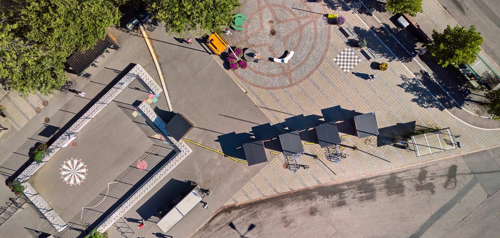 Aerial view of urban plaza with playground, trees, and circular paving pattern.