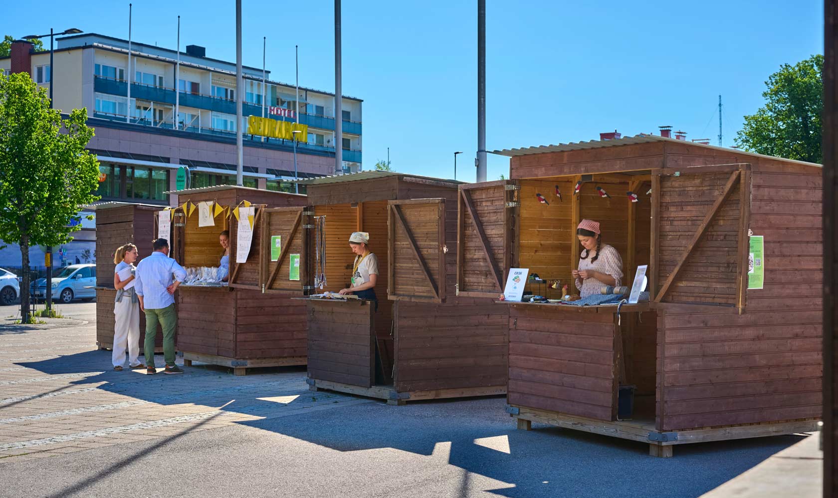 Outdoor market stalls with vendors and customers on a sunny city street.