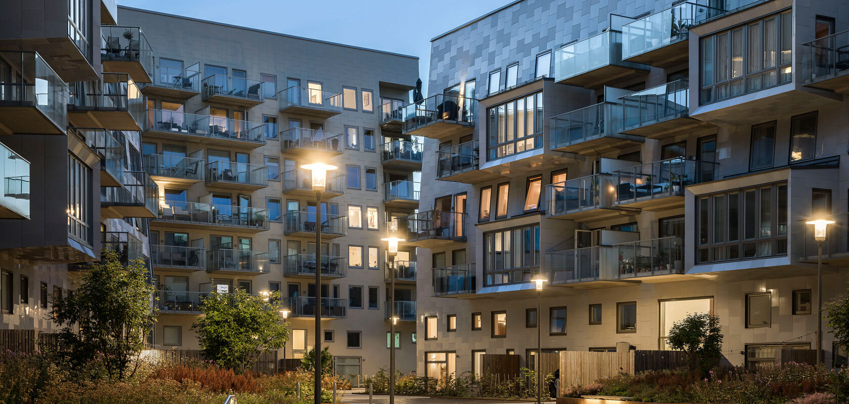 Modern apartment buildings with balconies at dusk in an urban courtyard with streetlights.
