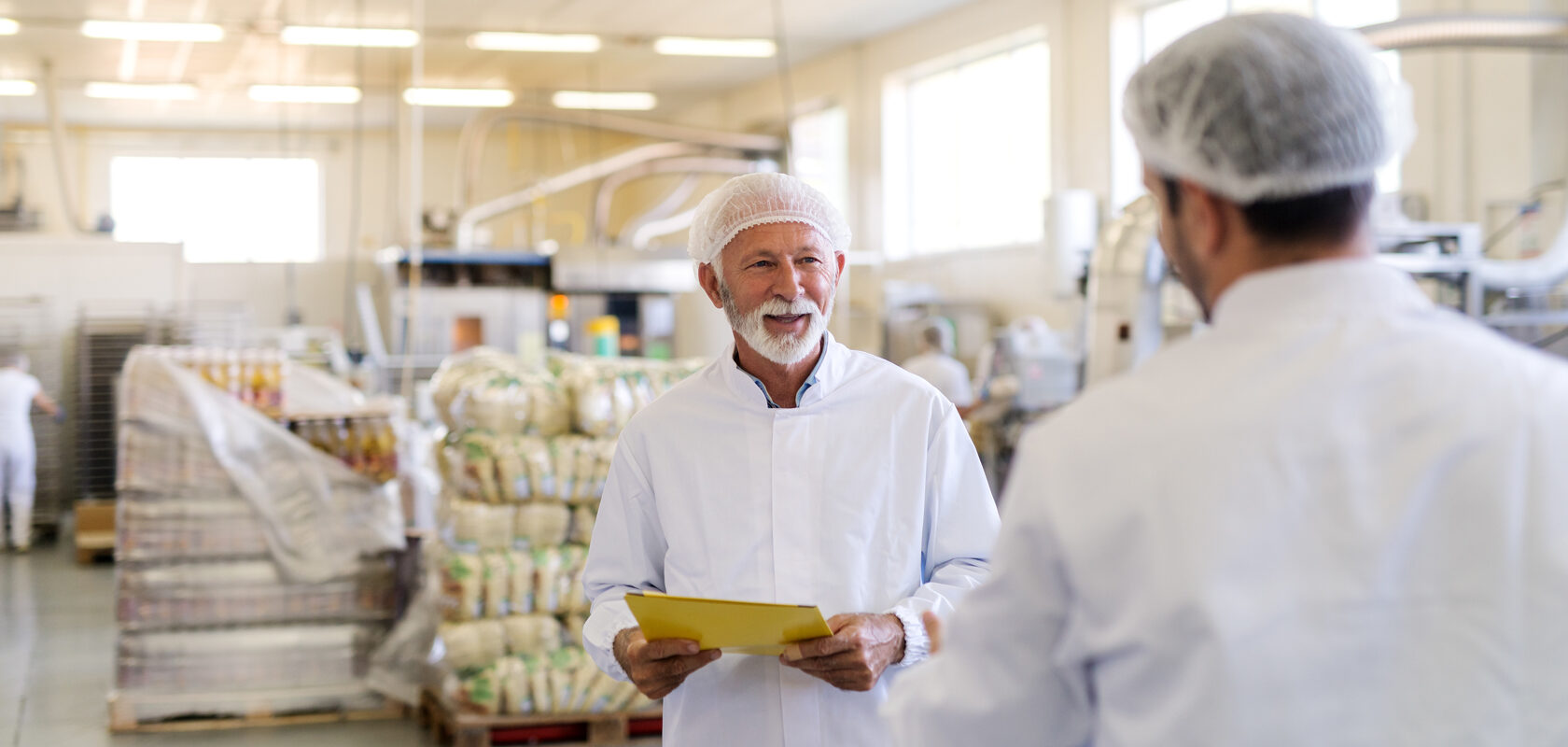 Food factory workers in hairnets and lab coats discussing quality control checklist.