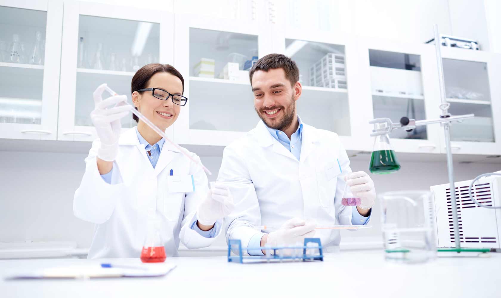 Two scientists in lab coats using pipette and flasks in a modern laboratory.